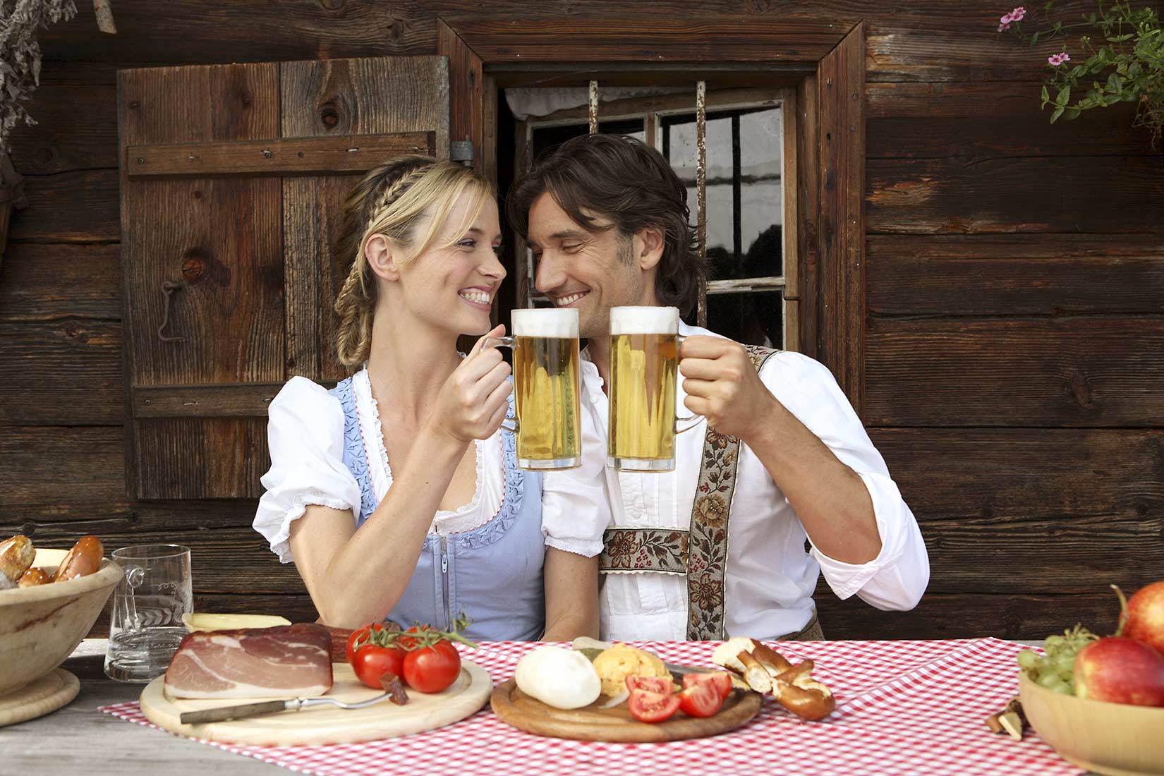 Das Paar in Tracht macht Brotzeit vor einer Almhütte. Brezen, Schinken, Obazda und ein frisch gekühltes Bier dürfen da nicht fehlen | NIKKY MAIER photo - 07