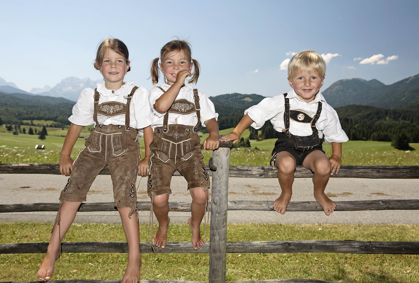 Drei Kinder in Lederhosen auf einem Holzzaun in den Bergen | NIKKY MAIER photo - 11